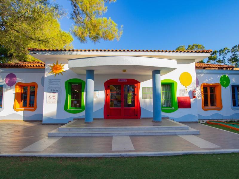 Edificio de hotel pintado de colores con columnas, ventanas y puertas coloridas en un jardín soleado.
