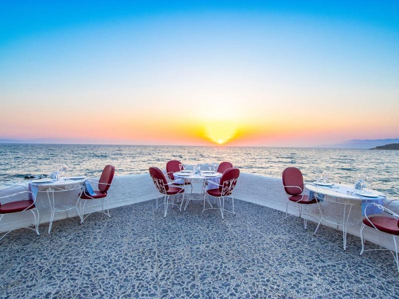 Terraza con mesas y sillas rojas con vista al mar al atardecer.