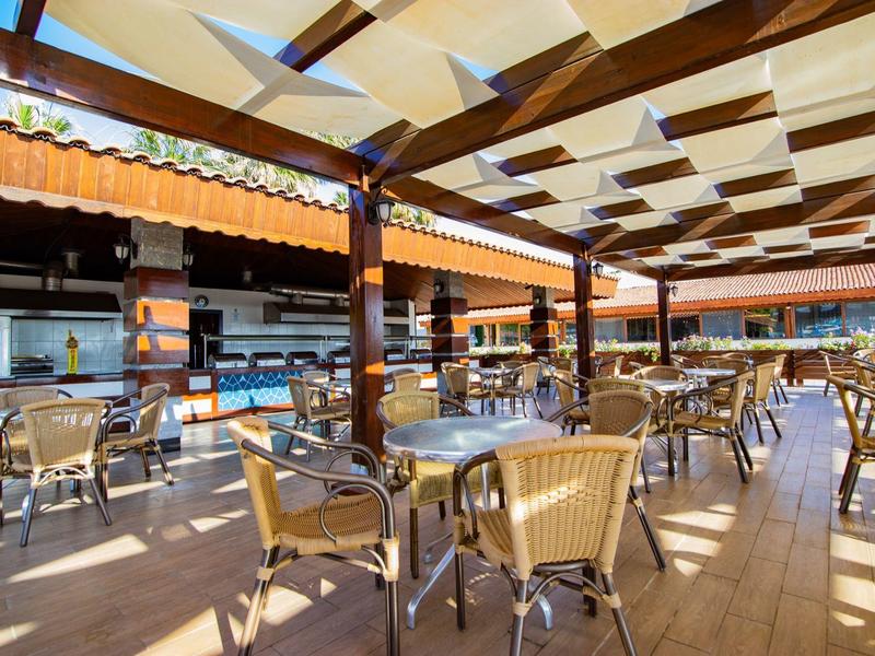 Zona al aire libre de un hotel con mesas, sillas y un toldo sombreado.