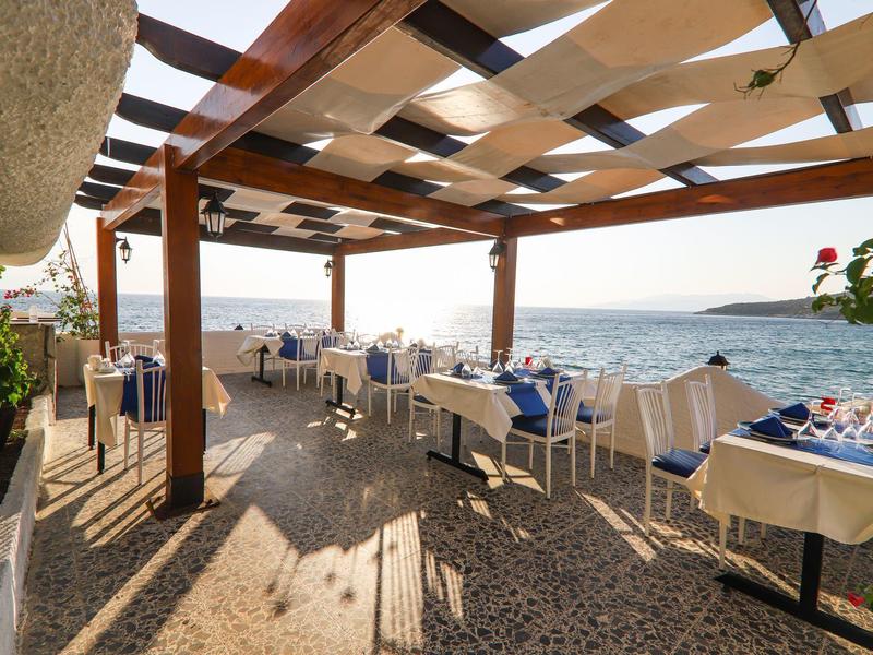 Terraza de restaurante con mesas y sillas bajo una lona con vista al mar