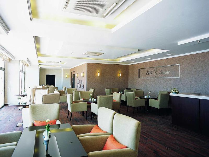 Heller, moderner Gastraum mit beigen Sesseln, dunklen Tischen und großen Fenstern an der linken Seite.