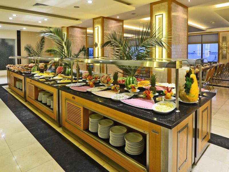 Buffet-Tisch mit vielfältigen Speisen, Obst und Geschirr in hellem, modernem Restaurant.