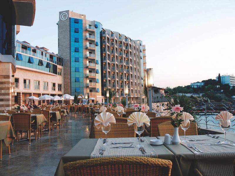 Große Terrasse mit gedeckten Tischen vor mehrstöckigen Gebäuden und klarem Himmel im Hintergrund.