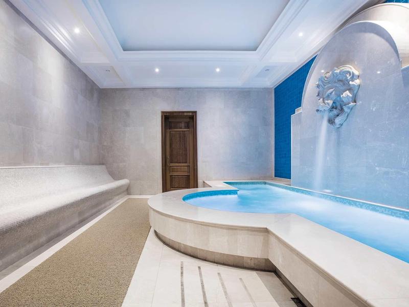 Moderner Spa-Bereich mit hellem Pool, grauen Wänden und gemütlicher Sitzbank.