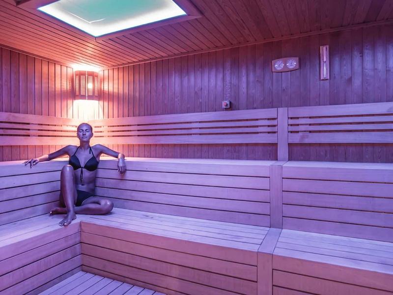 Leere Sauna mit Holzverkleidung, Holzbank und gedämpftem Licht an der Decke und der Wand.