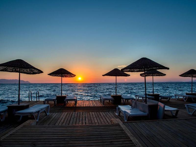 Sonnenuntergang am Meer mit Sonnenschirmen und Liegen auf einer Holzplattform.