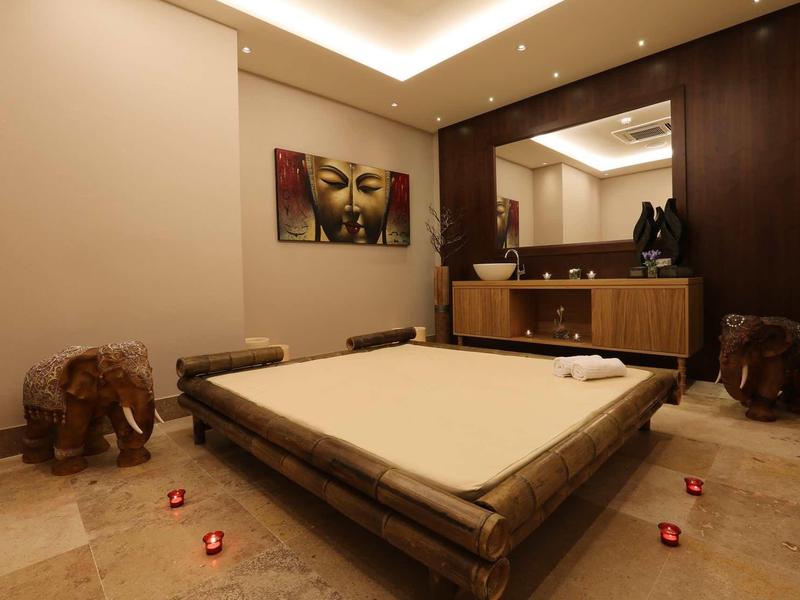 Zimmer mit niedrigem Bambusbett, zwei Holz-Elefantenhockern, warmen Wänden und Buddha-Bild.