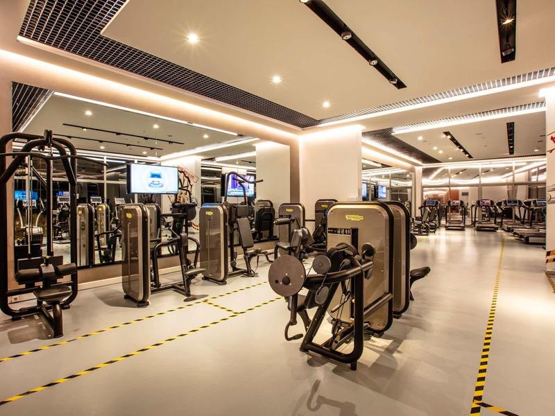 Großer moderner Fitnessraum mit mehreren Kraftgeräten, hellen Wänden und integrierter Deckenbeleuchtung.