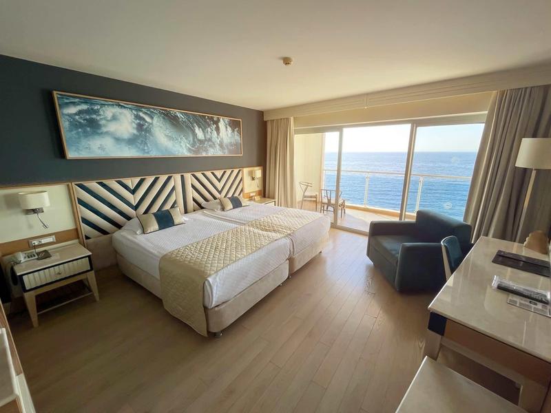 Modernes Hotelzimmer mit zwei Einzelbetten, Schreibtisch, Sessel und großer Fensterfront mit Meerblick.