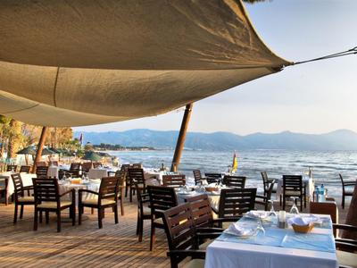 Terrassenrestaurant mit Holztischen und weißen Tischdecken am Meer bei Sonnenuntergang.