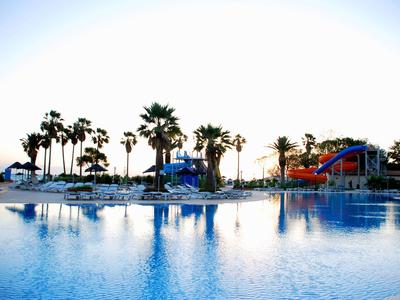 Blick auf einen großen Pool mit Wasserrutschen und Palmen bei Sonnenuntergang.