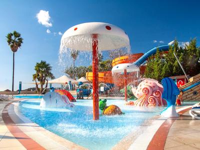 Farbiger Wasserspielplatz mit Pilz-Sprinkler, Rutschen und Palmen bei Sonnenschein.