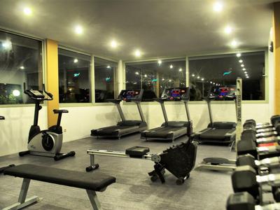 Helles Fitnessstudio mit Laufbändern, Fahrrädern und Hanteln neben großen Fenstern.