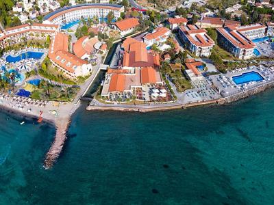 Luftaufnahme eines Küstenresorts mit roten Dächern, mehreren Pools und klarem blauem Meer.