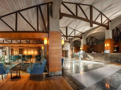 Große Hotellobby mit Holzdeckenbalken, Marmorboden, Sitzgruppen und warmem Licht.