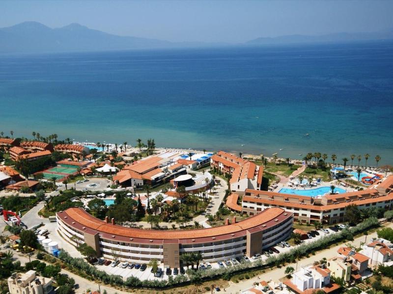Luftaufnahme eines Küstenresorts mit gebogenen Gebäuden, Schwimmbädern und blauem Meer im Hintergrund.