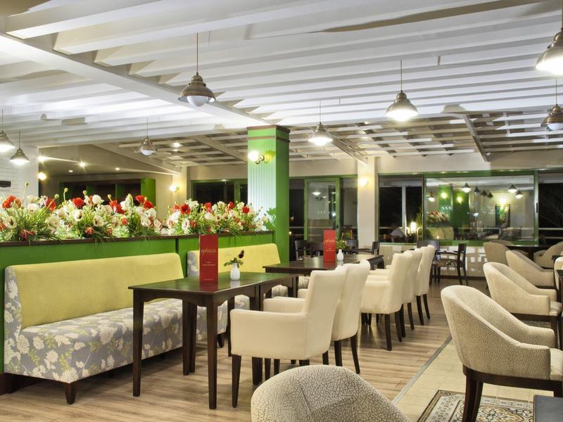 Modernes Restaurant mit grünen Akzenten, bequemen Stühlen und blumiger Dekoration bei hellem Licht.