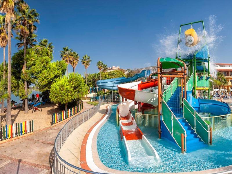 Wasserpark mit bunten Rutschen, Palmen und blauem Himmel am sonnigen Tag.