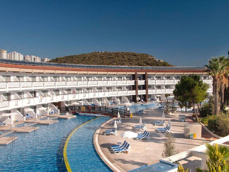 Großes Hotel mit geschwungenem Pool, weißen Liegen und Palmen unter klarem blauem Himmel.