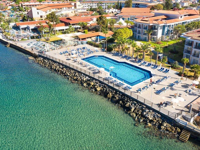 Hotelanlage mit Swimmingpool und Sonnenschirmen an klarer Küste mit türkisblauem Wasser.