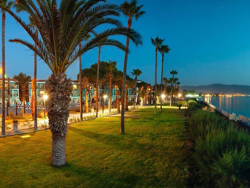 Uferpromenade bei Abenddämmerung mit Palmen, beleuchtetem Weg und ruhigem Wasser.
