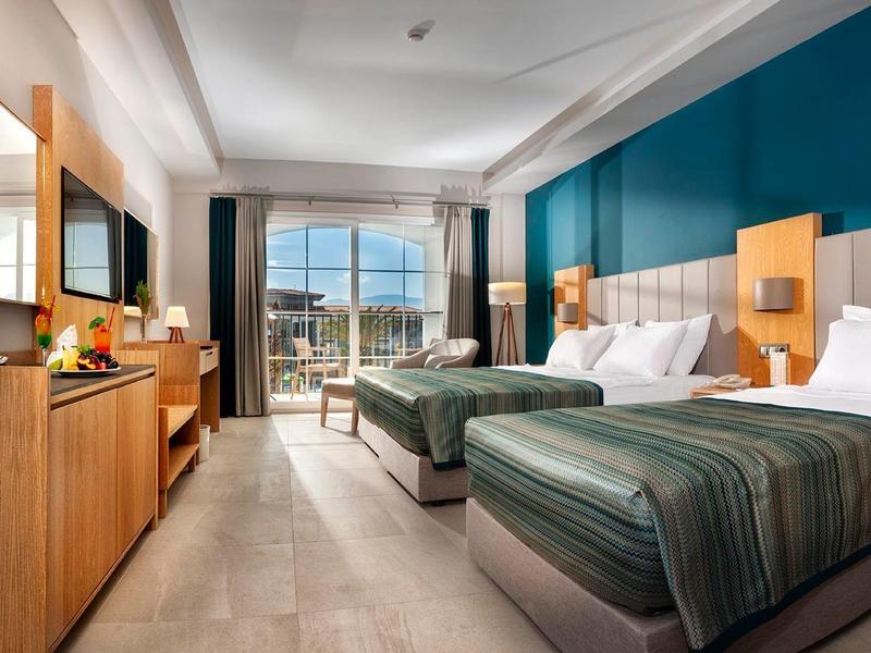 Modern eingerichtetes Hotelzimmer mit zwei Einzelbetten, Holzmöbeln und Balkon mit Meerblick.