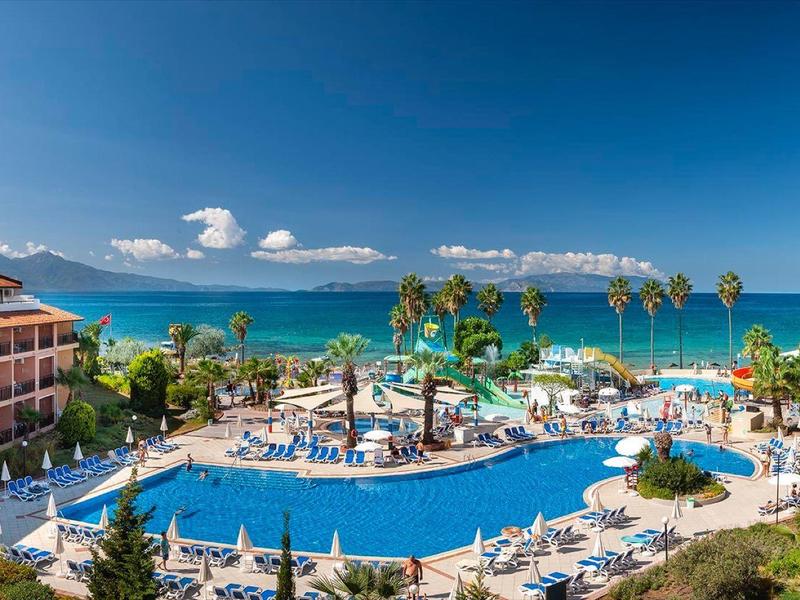 Großes Hotel mit zwei Gebäuden, großem Pool, Palmen und Blick auf das blaue Meer bei klarem Himmel.