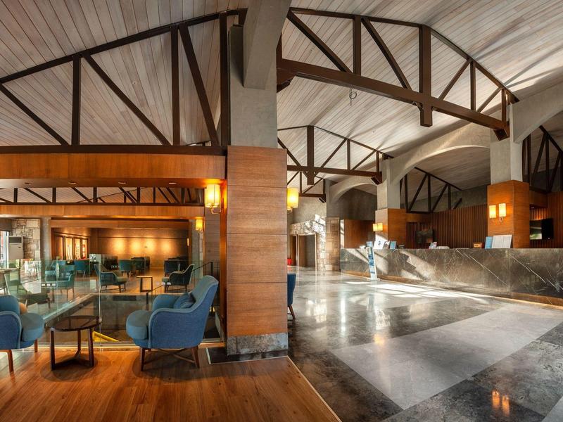 Große Hotellobby mit Holzdeckenbalken, Marmorboden, Sitzgruppen und warmem Licht.