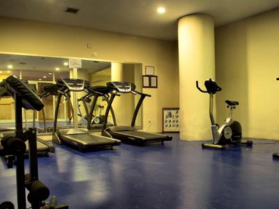 Palestra con tapis roulant, cyclette e manubri su pavimento blu.