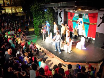 Persone su un palco che si esibiscono di fronte a un grande pubblico all'aperto la sera.