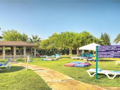 Giardino verde con lettini e ombrellone davanti a un edificio sotto un cielo sereno.