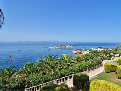 Blick auf das blaue Meer mit Palmen, grünen Büschen und klarem Himmel am Küstenweg.