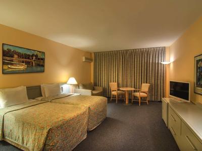 Geräumiges Hotelzimmer mit zwei Betten, beige Wänden, Vorhängen und Sitzecke mit Tisch.