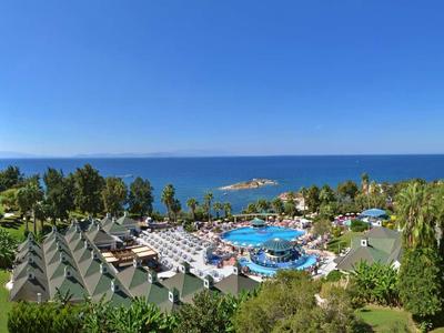 Panorama eines Hotels mit Pool, Garten und Blick auf das Meer bei klarem Himmel.