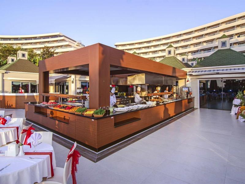 Offener Außenbereich mit Buffet, gedeckten Tischen und großen weißen Gebäuden im Hintergrund.