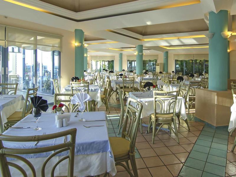 Großer, heller Speisesaal mit vielen gedeckten Tischen, Stühlen und großen Fenstern.