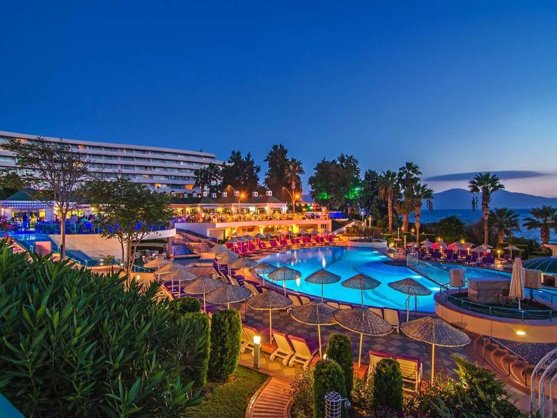 Hotelanlage mit beleuchtetem Pool, Liegen, Palmen und klarem Abendhimmel am Meer.