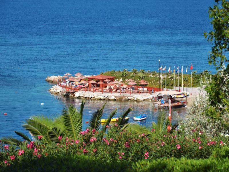 Kleiner Badebereich mit Liegestühlen, Sonnenschirmen und Booten am klaren blauen Meer.