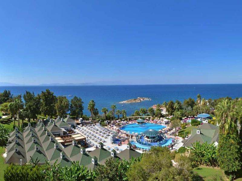 Großes Hotelresort mit blauem Pool, Palmen, grünen Gärten und Blick aufs blaue Meer.