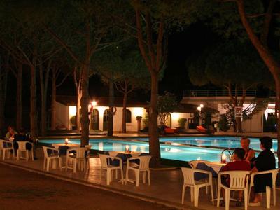 Beleuchteter Pool bei Nacht mit weißen Plastikstühlen und Bäumen im Hintergrund.