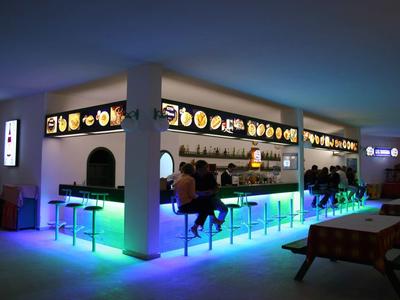 Moderne Bar mit leuchtender blauer LED-Beleuchtung und Sitzplätzen, Menschen sitzen und unterhalten sich.