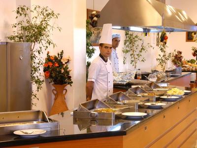 Küchenchef in weißer Uniform vor warmem, modernem Buffet mit großen Chrombehältern und Pflanzen.