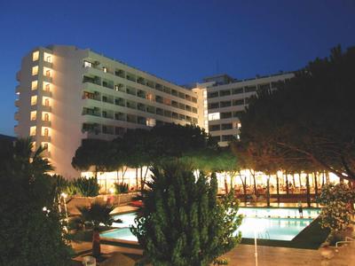 Ein beleuchtetes Hotelgebäude mit Schwimmbad und Bäumen in der Dämmerung.