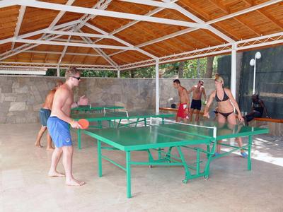 Meerdere mensen spelen tafeltennis in een overdekte, open ruimte met een groene tafel.