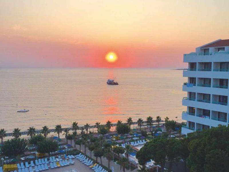 Sonnenuntergang am Meer mit Hotel, Pool, Palmen und mehreren Booten auf dem Wasser.