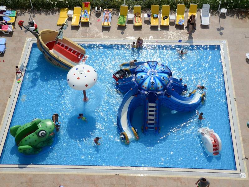 Großes Kinderbecken mit bunten Wasserrutschen, Spielfiguren und gelben Liegestühlen drumherum.