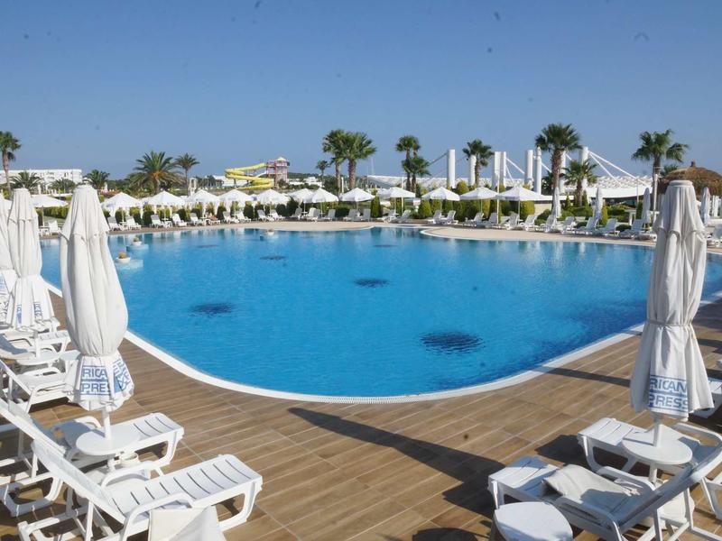 Großer runder Pool mit weißen Liegestühlen und Sonnenschirmen auf braunem Holzboden.