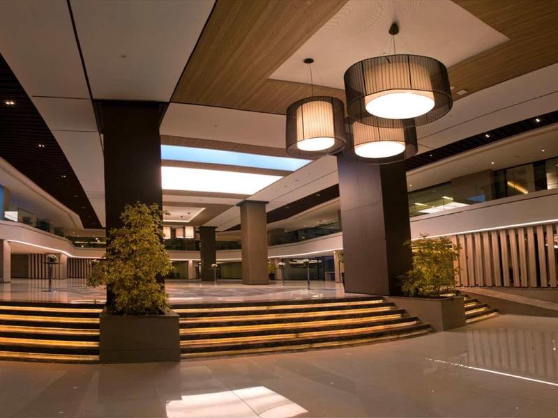 Moderne, offene Lobby mit Holzdecken, indirekter Beleuchtung und großen Glasflächen bei Sonnenlicht.