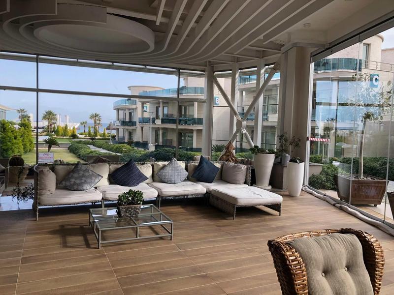 Große, helle Terrasse mit gemütlicher Eckcouch, Glaswänden und Blick auf moderne Gebäude.