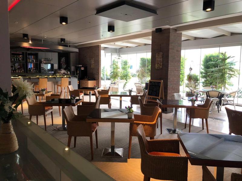 Helles Café mit Holztischen, gemischten Stühlen und großen Fenstern zum Garten.